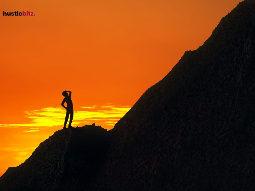 Silhouette of a person standing on a mountain at sunset.