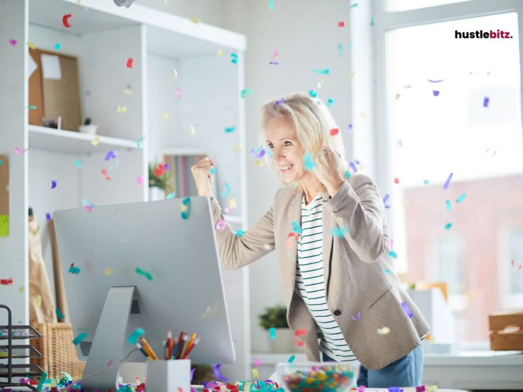 A woman celebrating in front of her computer as confetti falls.