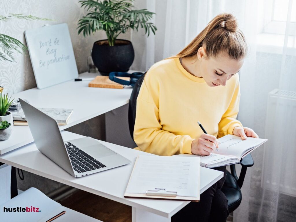 A woman doing writing and a laptop in the table