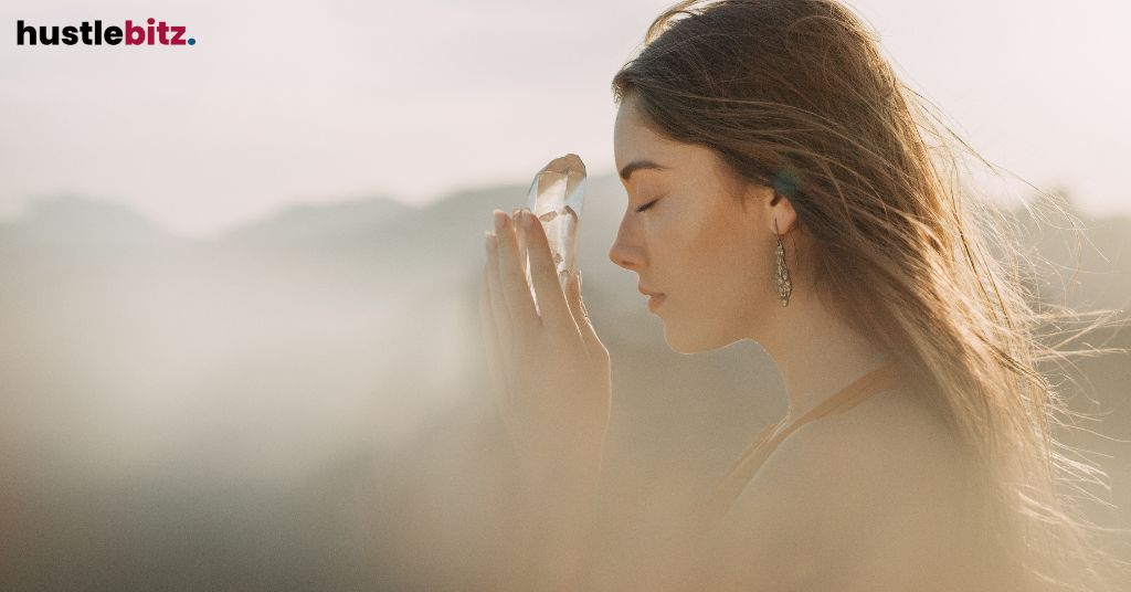 Woman with eyes closed holding a crystal in a serene, sunlit setting.