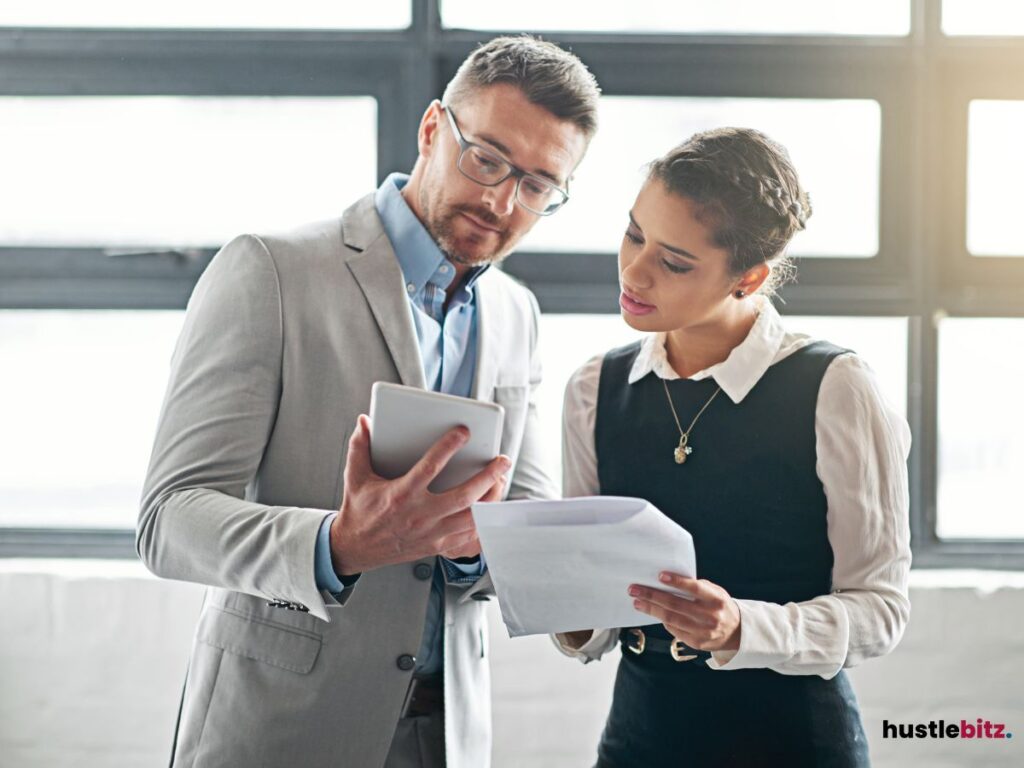 A man and woman discussing while looking at a tablet and document.