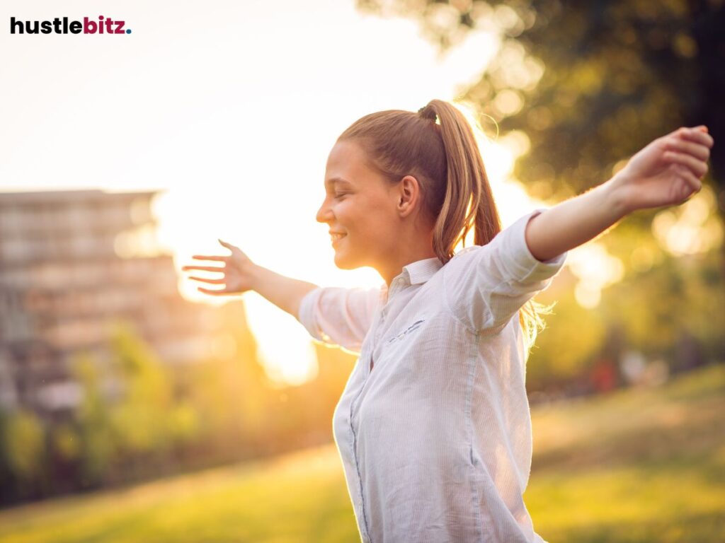 A woman standing in the sunlight with arms outstretched.