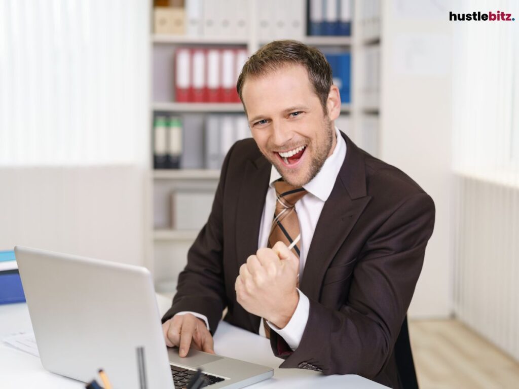 A man in a suit excitedly celebrates while working on a laptop.