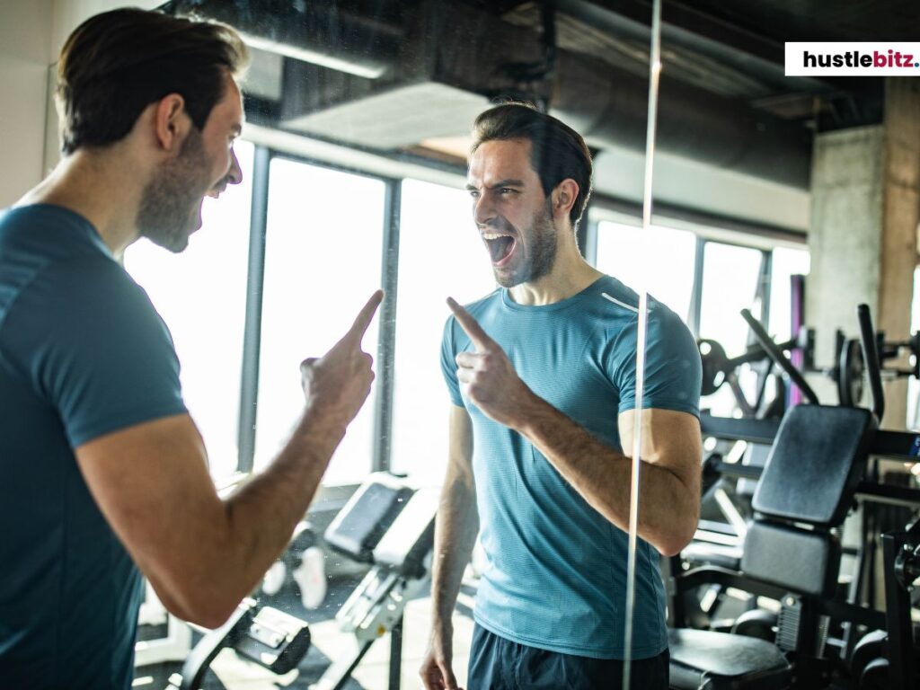 A man in a gym mirror laughing and pointing at his reflection.