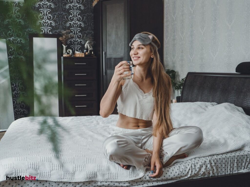 A woman drinking water in the bed and smiles