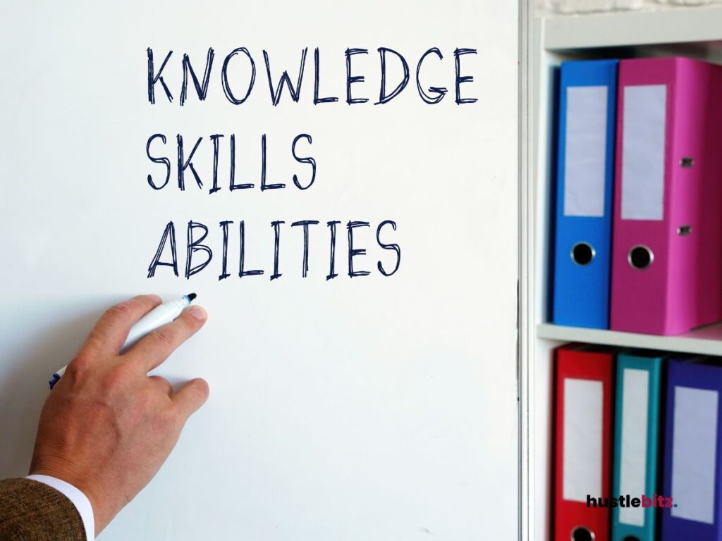 A hand writes "KNOWLEDGE, SKILLS, ABILITIES" on a whiteboard with colorful binders in view.