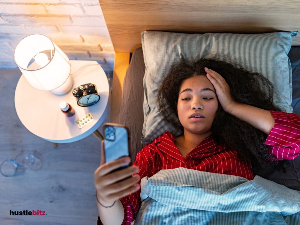 A woman in bed, checking her phone, looking tired.