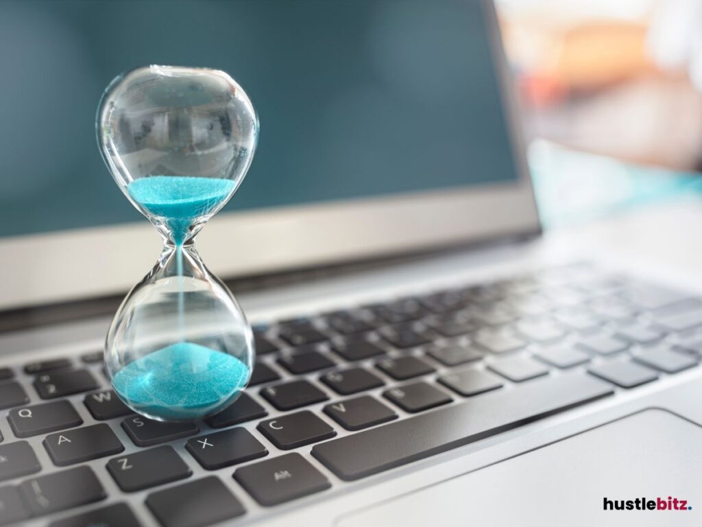 An hourglass with blue sand on a laptop keyboard.