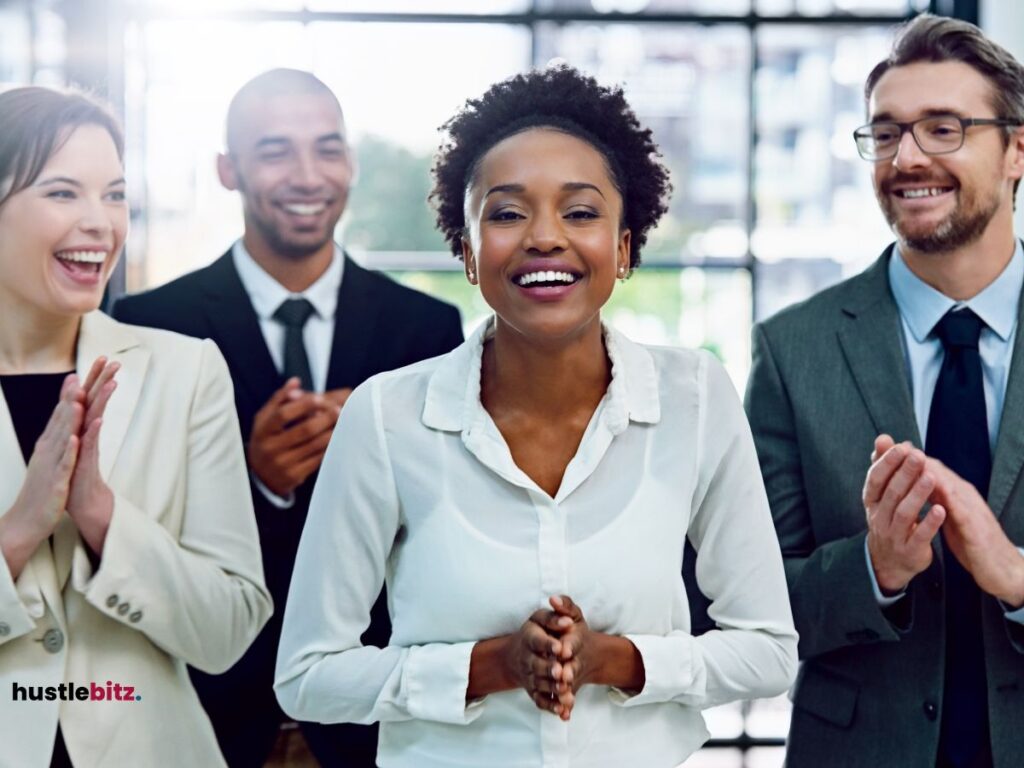 A group of professionals smiles and claps, focusing on a woman in the center.