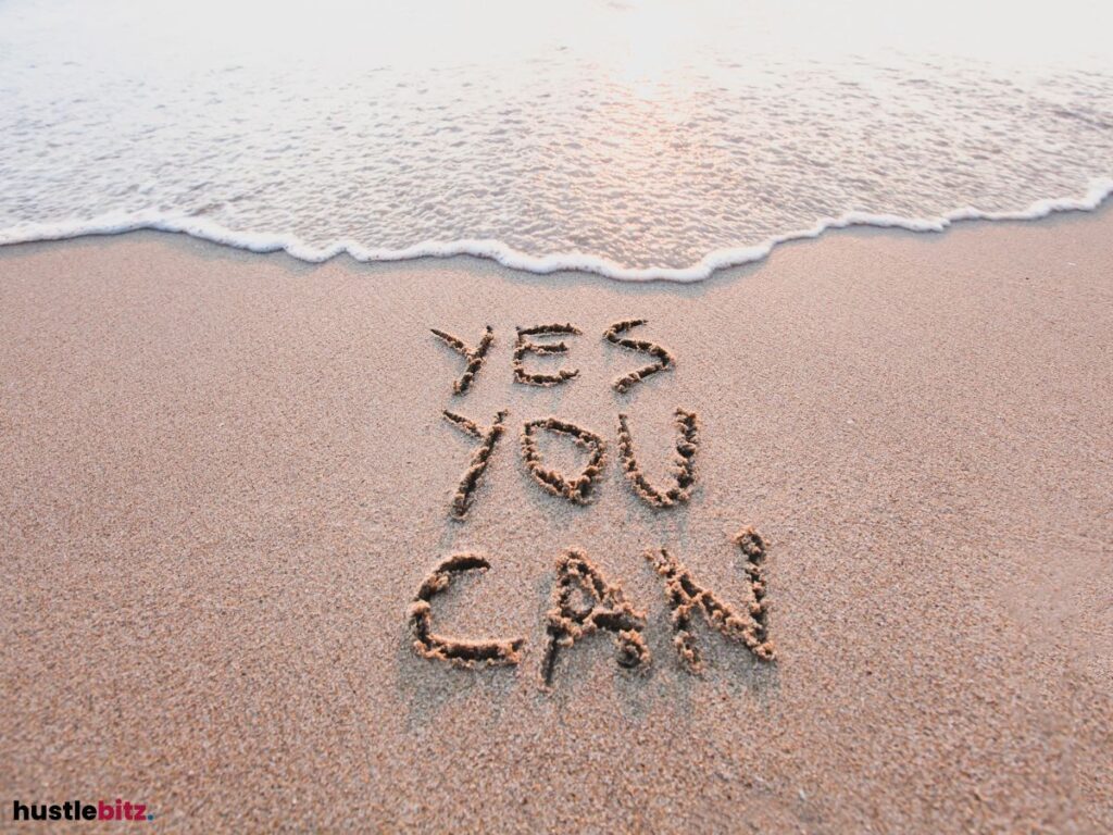 "YES YOU CAN" written in the sand near the shoreline, with ocean waves approaching.