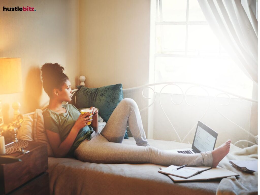 A woman lounging on her bed, looking out the window with a cup of coffee.