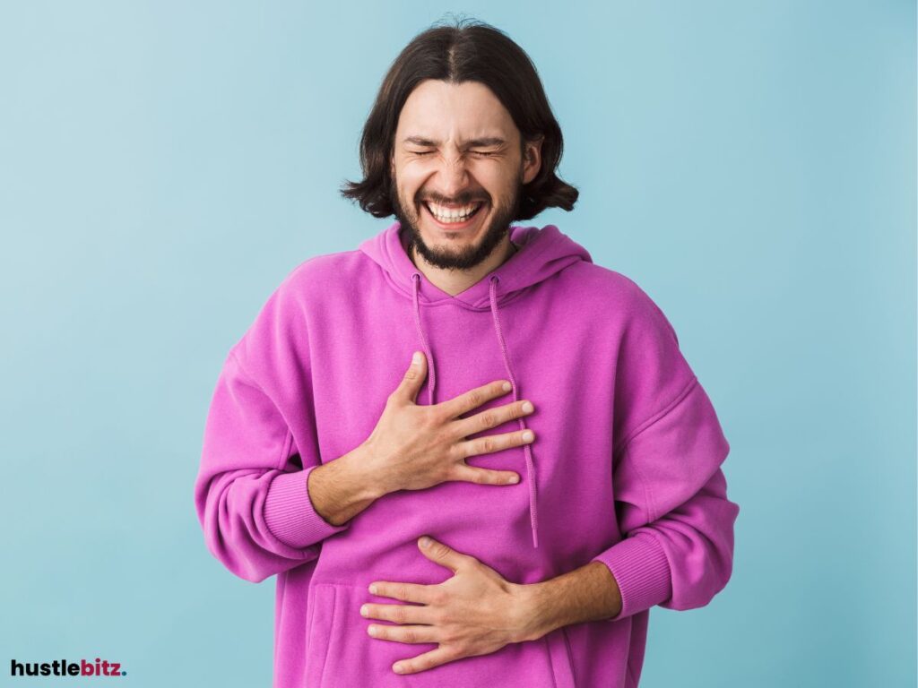 A man in a purple hoodie laughing with his hand on his chest.