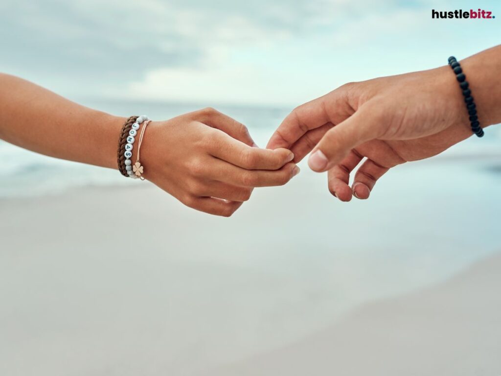 Two hands gently touching, fingers barely connecting by the beach.