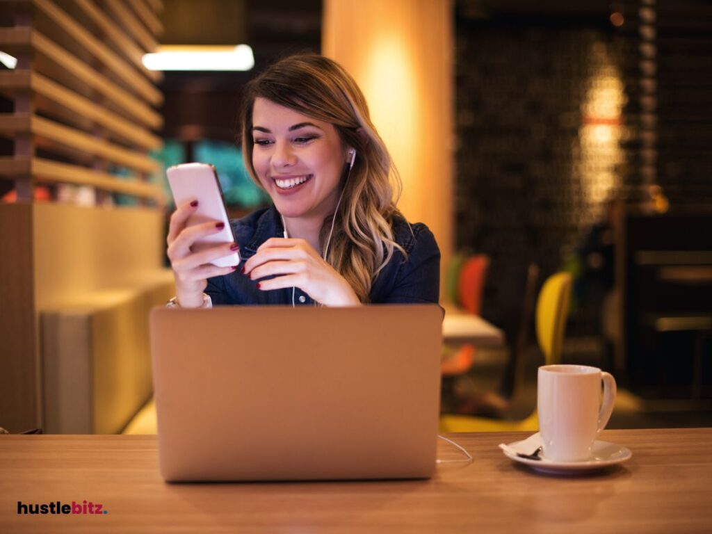 A woman smiles while using cellphone and a laptop in the table