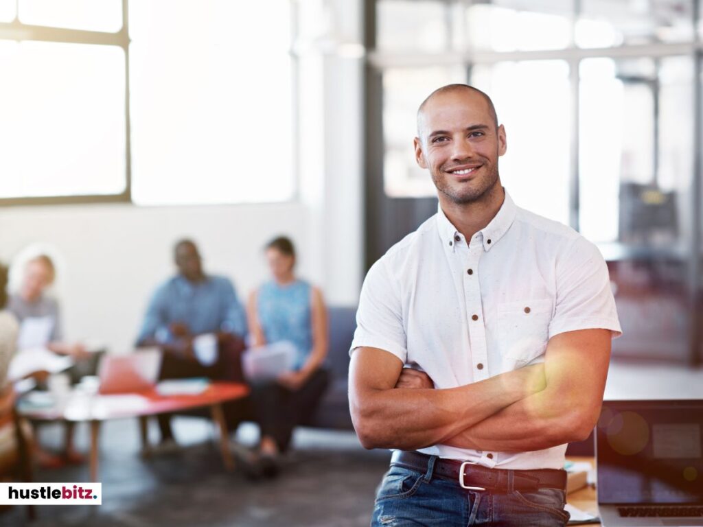 A man in a white shirt smiles confidently, arms crossed, in an office setting.