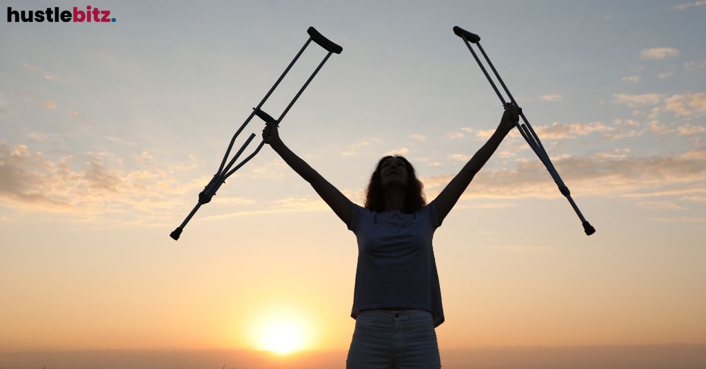 A person holding crutches in the air triumphantly at sunset.