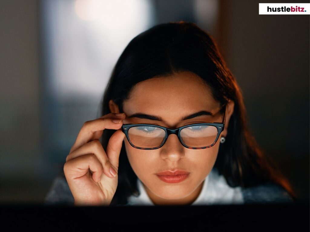 A focused woman adjusting her glasses, staring intently at a computer screen.