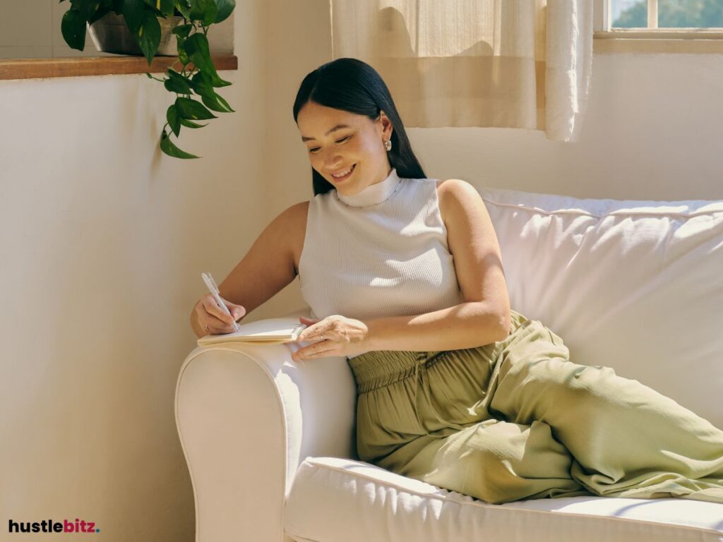 Woman writing in a journal, smiling while sitting on a couch.