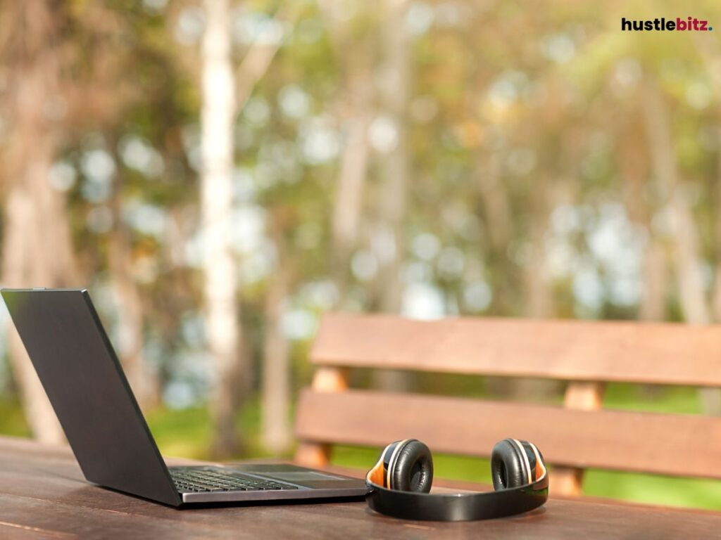 A laptop and headphones placed on a wooden outdoor bench.