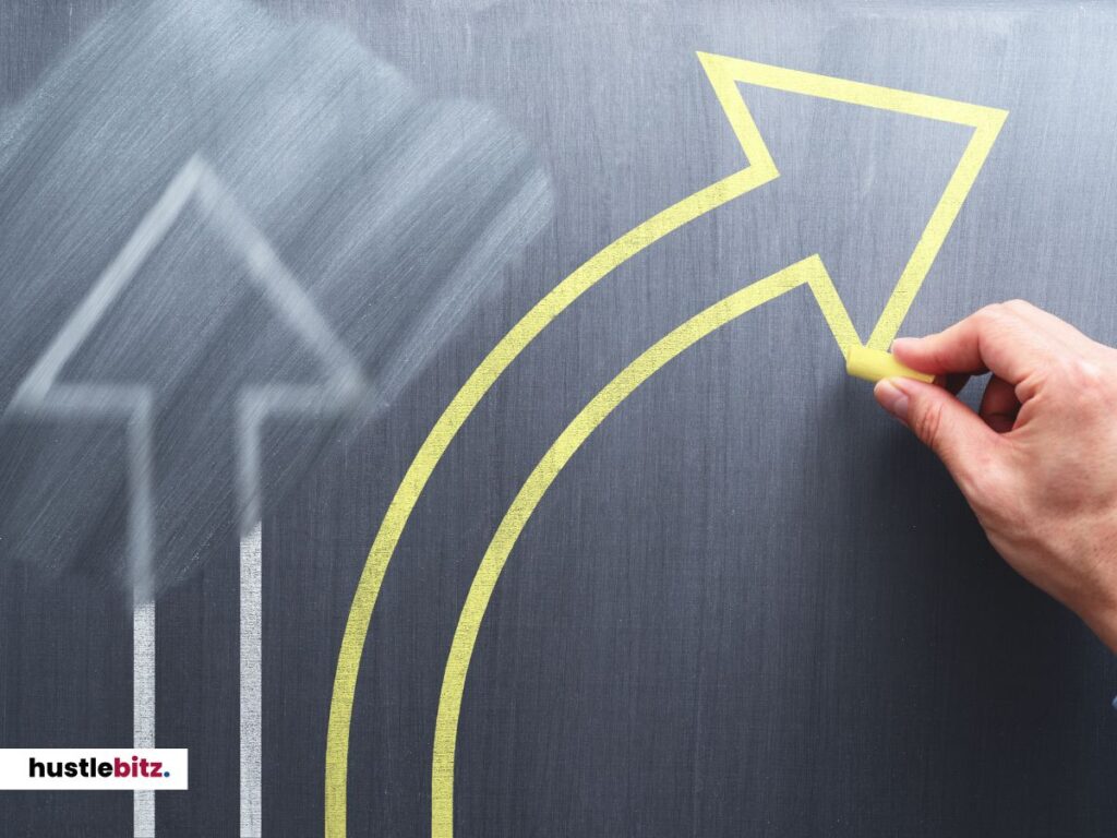 A hand drawing a bold yellow arrow on a chalkboard, curving upward from a faded path.