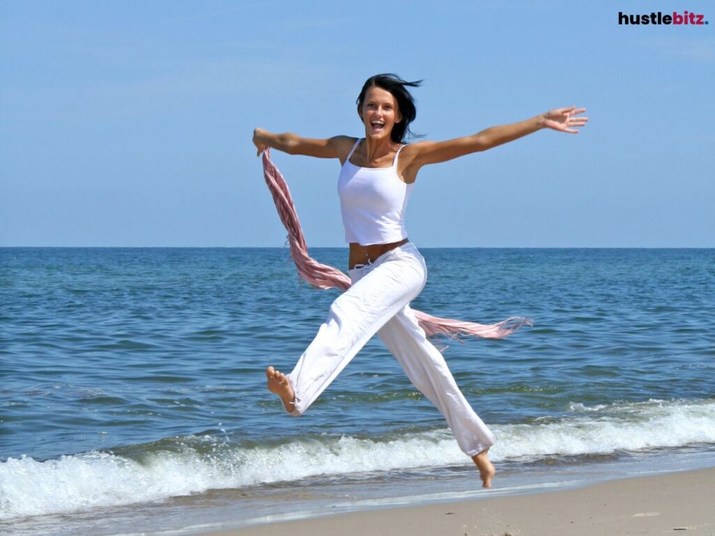 A woman happily jumps in the seashore.