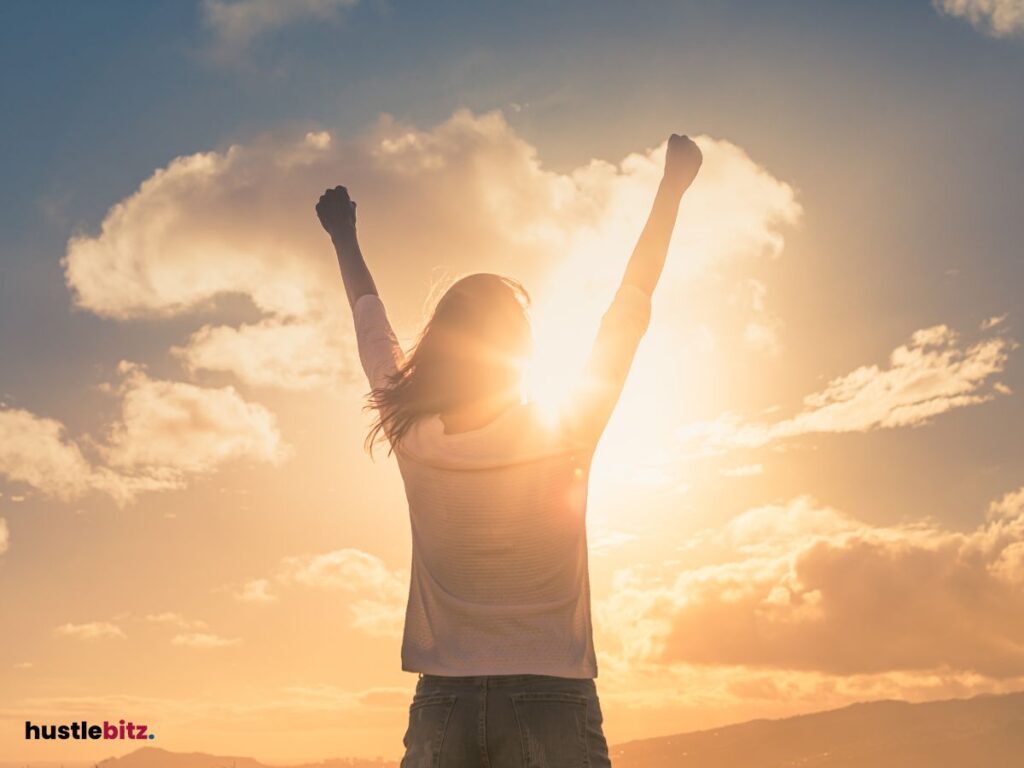 A woman facing the sun with raised arms, basking in golden sunlight.