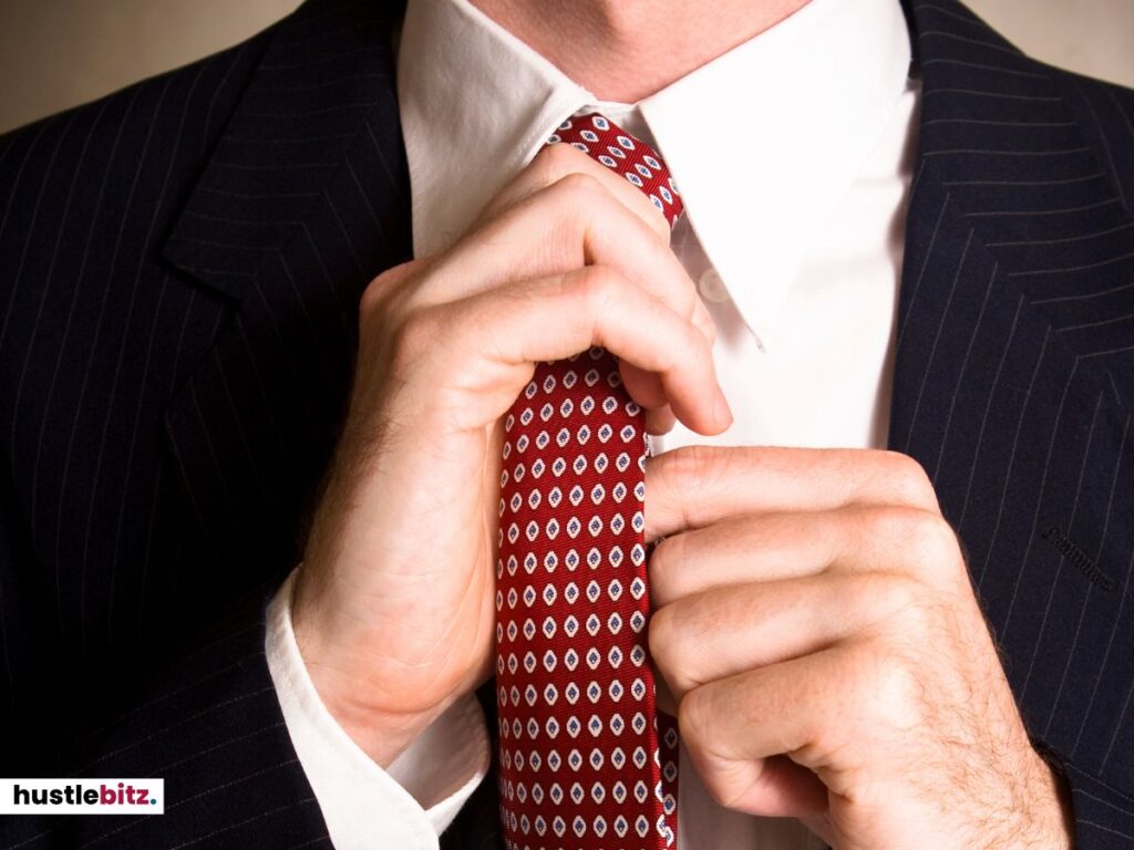 Close-up of a man adjusting his red tie in a business suit.