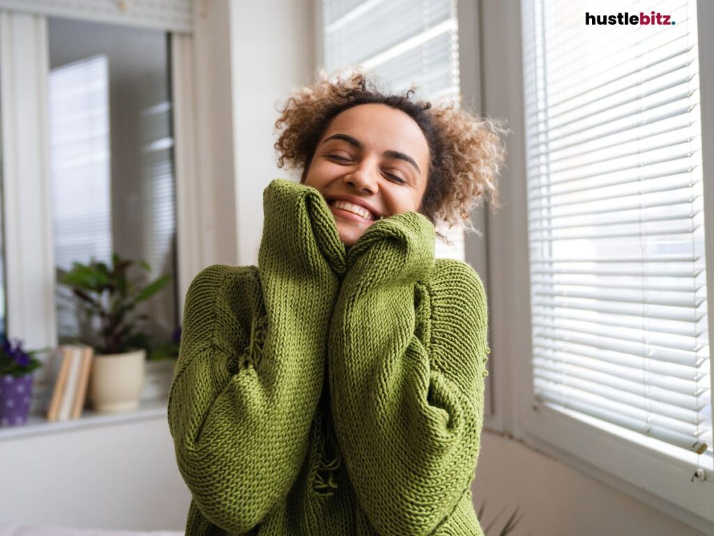Smiling woman in a green sweater, holding it up to her face in joy.