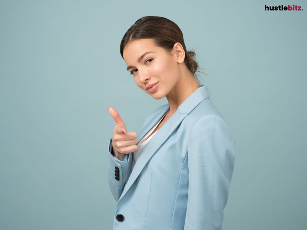 A woman pointing confidently while smiling, against a plain background.