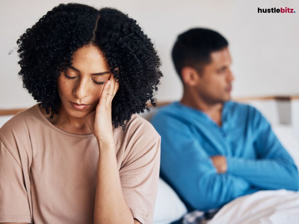 A woman looking distressed while a man sits in the background.