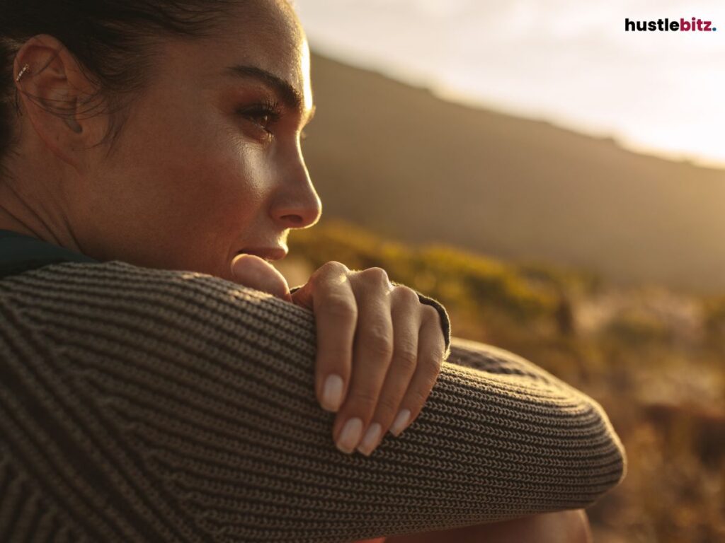 Close-up of a woman outdoors, resting her chin on her arms, deep in thought.