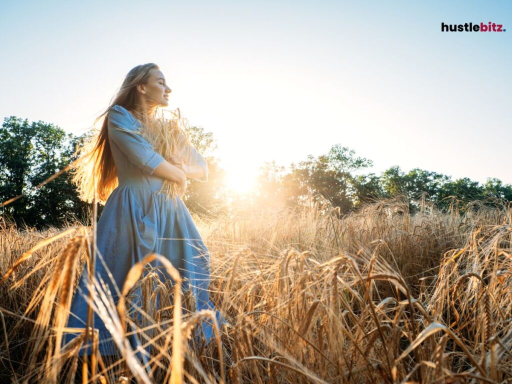 Woman standing in a wheat field at sunset, embracing nature and peace.