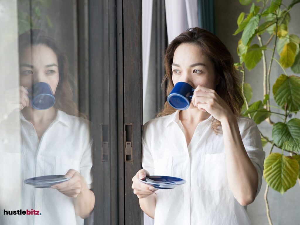 Woman sipping coffee, calmly looking outside a window.