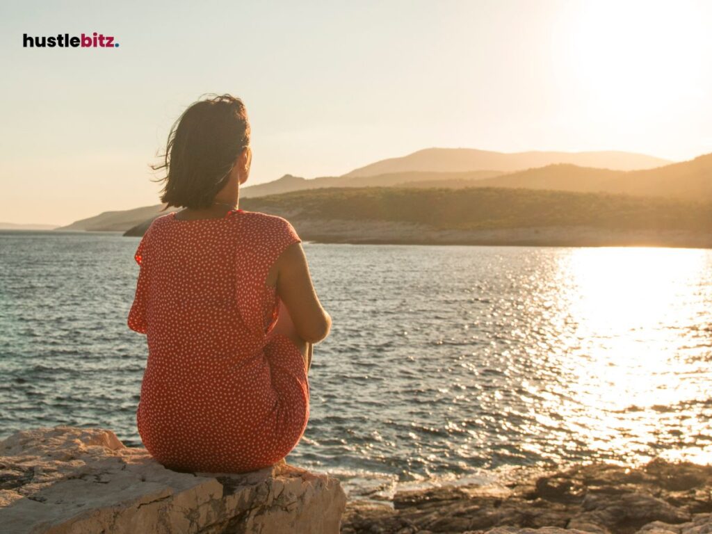 Woman sitting on a rock, watching the serene sea at sunset.