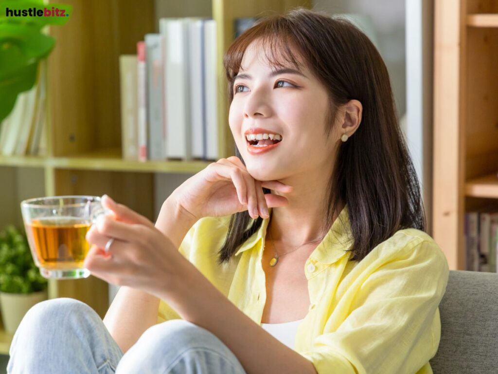 Woman smiling and drinking tea while sitting comfortably.