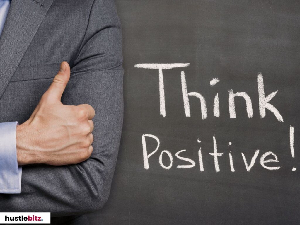 A person giving a thumbs-up in front of a chalkboard that says "Think Positive!"