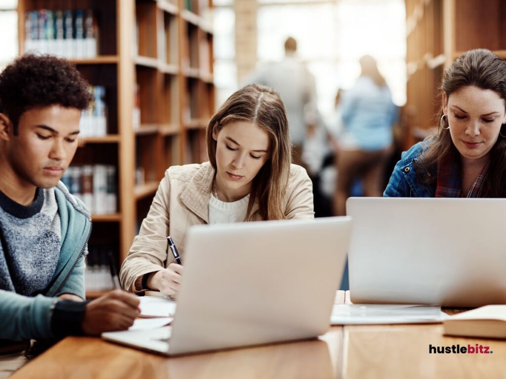 three people doing writing in front of the laptop inside the library