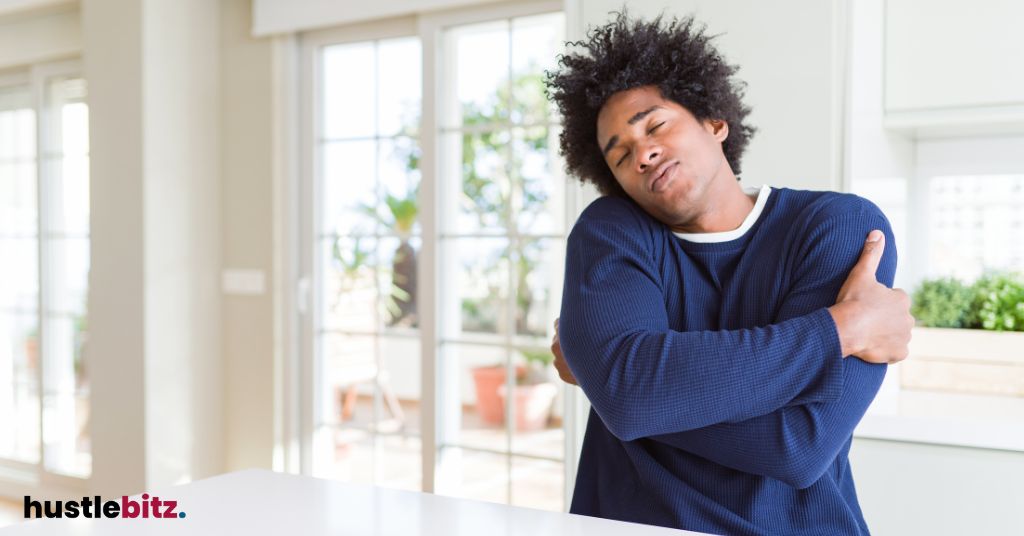 Man hugging himself, in a cozy home environment.
