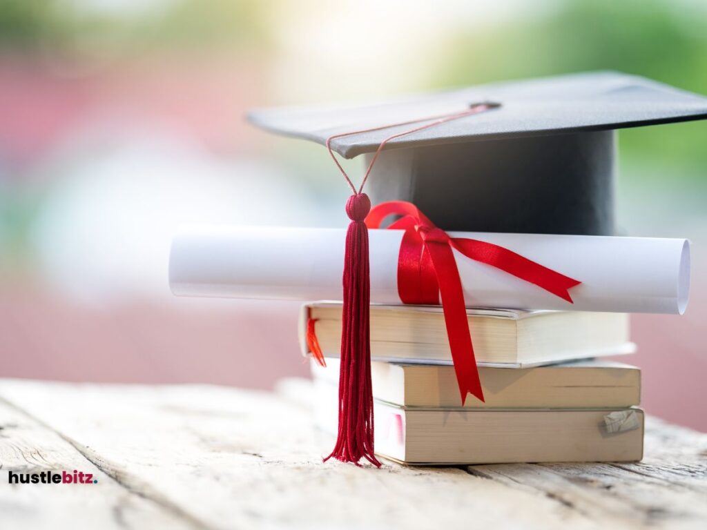 A graduation cap and diploma with a red ribbon are placed on a stack of books.