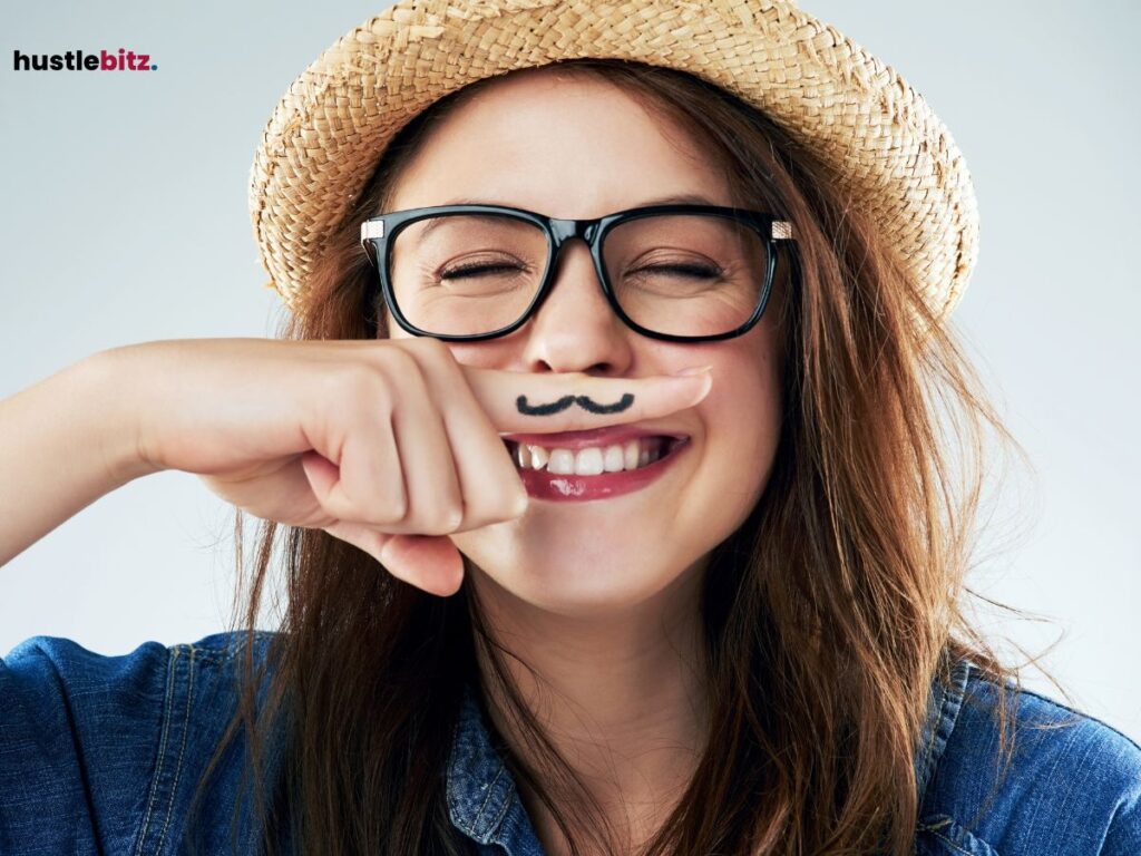 A woman smiling playfully with a mustache drawn on her finger.