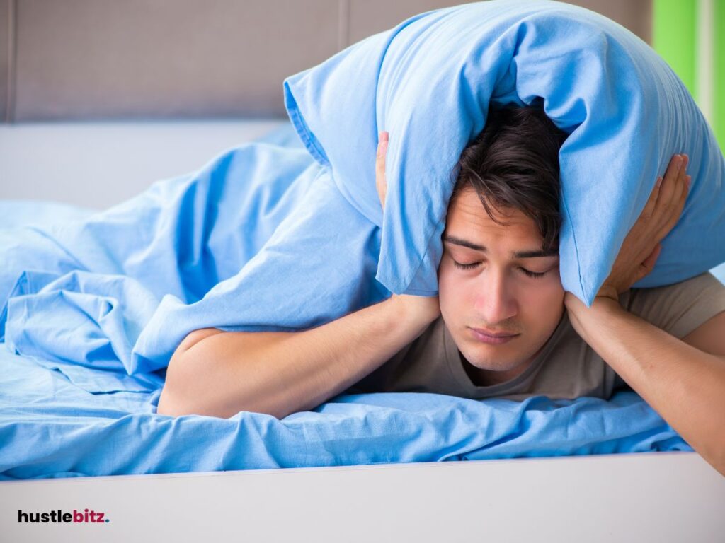 A man covering his ears with a pillow, struggling to sleep.