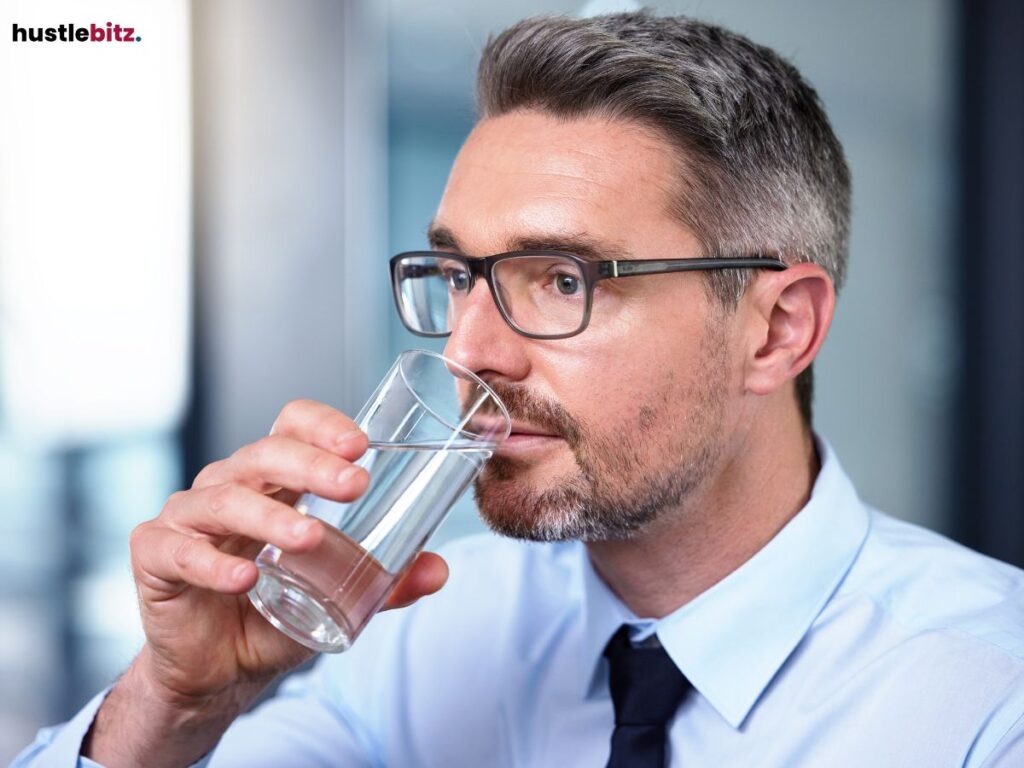Businessman sipping water from a glass in a professional setting.