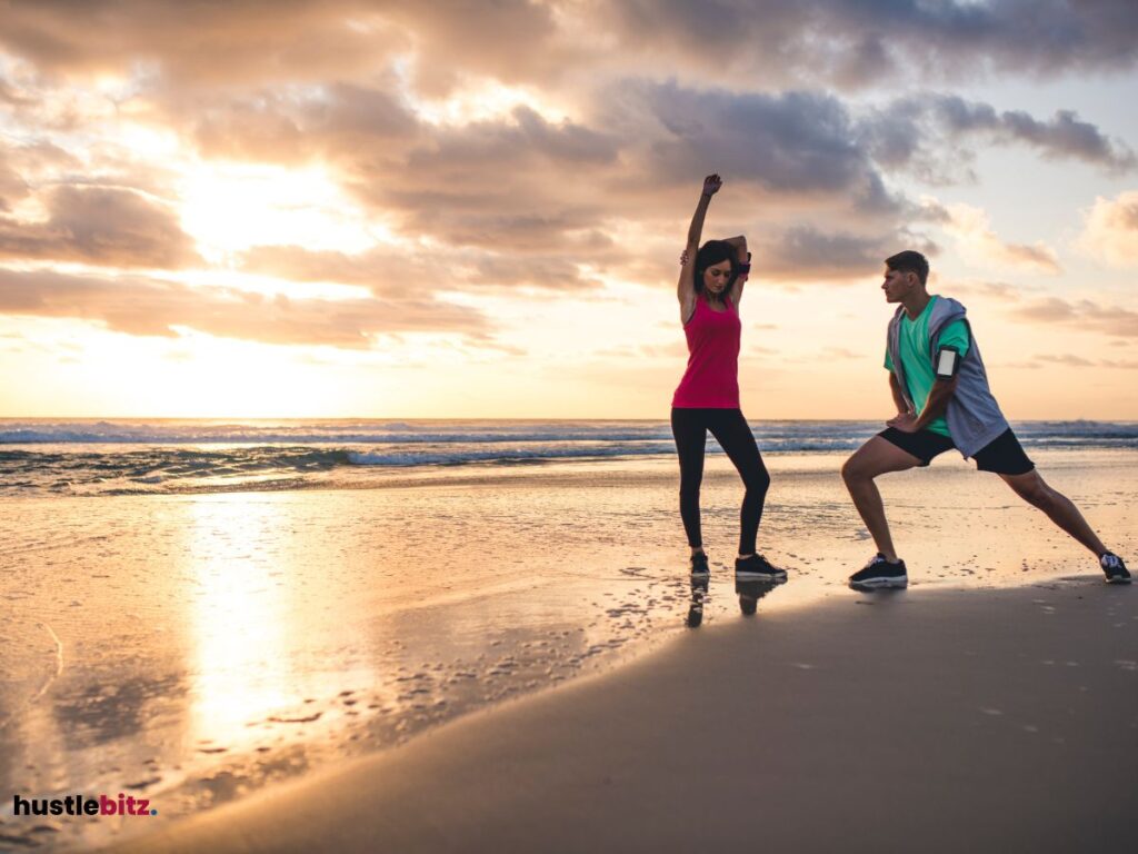 Two people stretching on a beach at sunset.