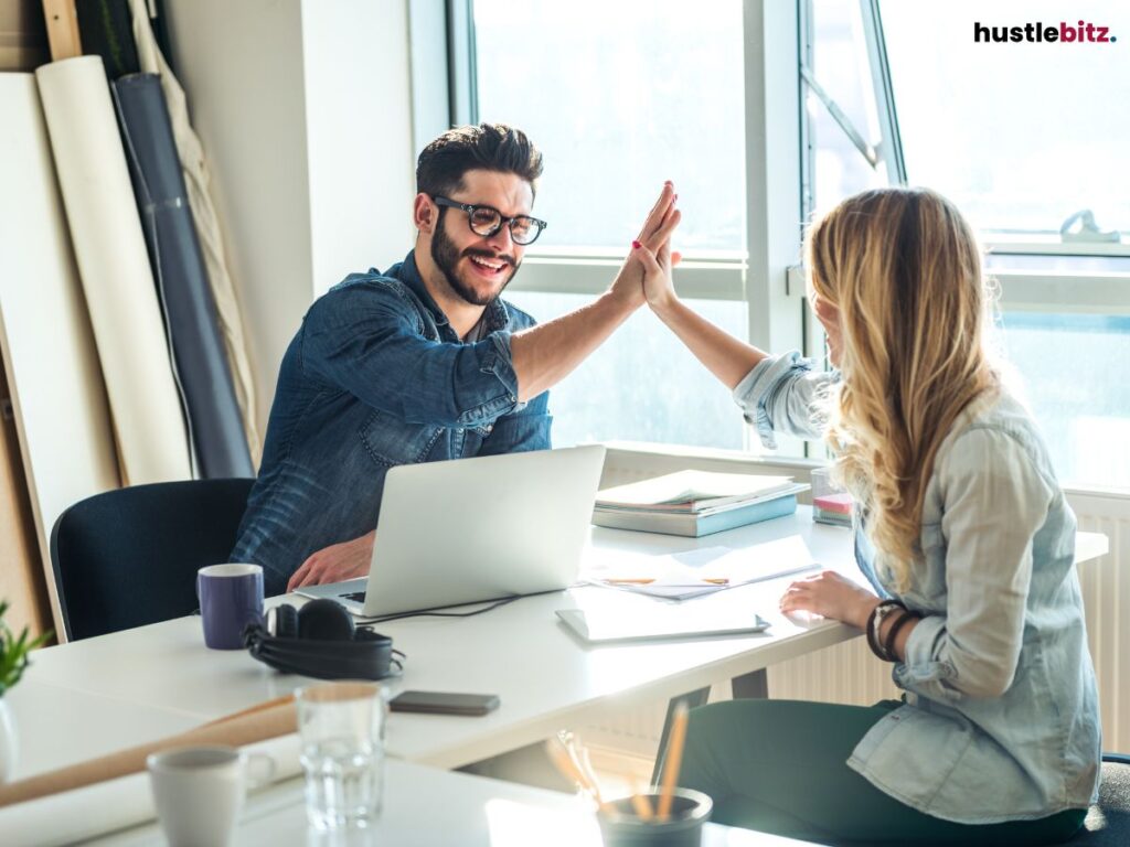 Two colleagues giving a high-five while sitting at a desk.