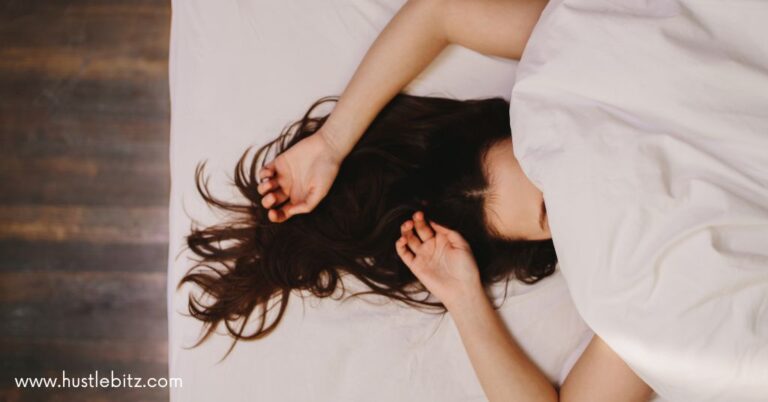 A woman lying in bed with a blanket covering her head.