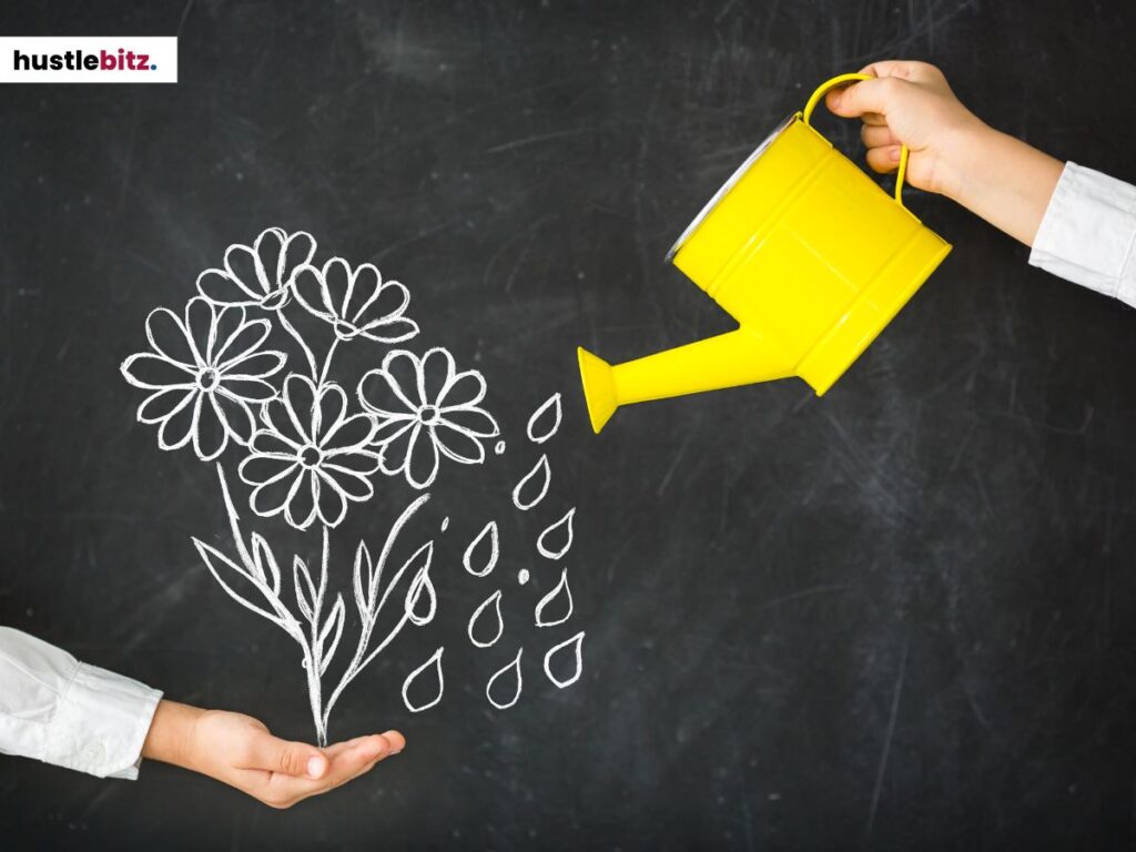 A hand holding a yellow watering can and a chalk-drawn flowers on a blackboard.