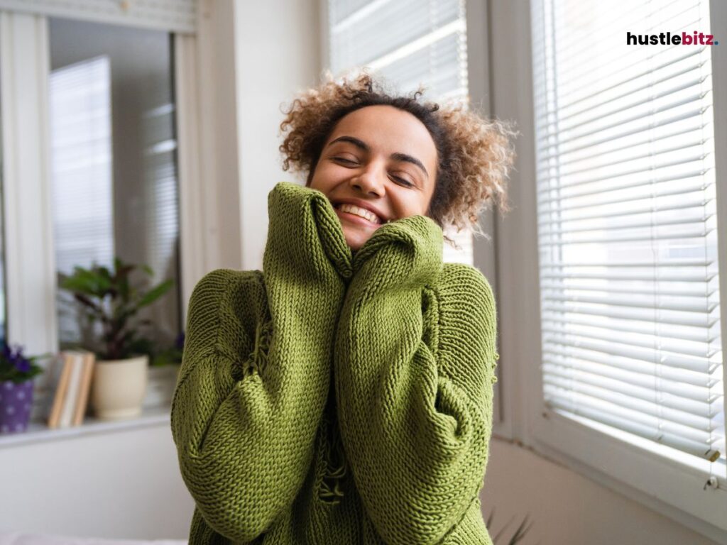A woman wearing a cozy green sweater, hugging herself with a big smile