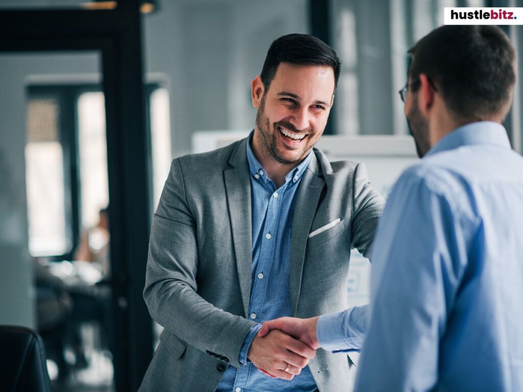Two businessmen smiling and shaking hands in an office environment.