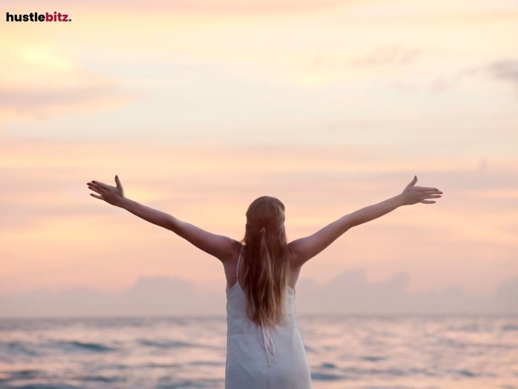 Woman with open arms facing the ocean at sunset.