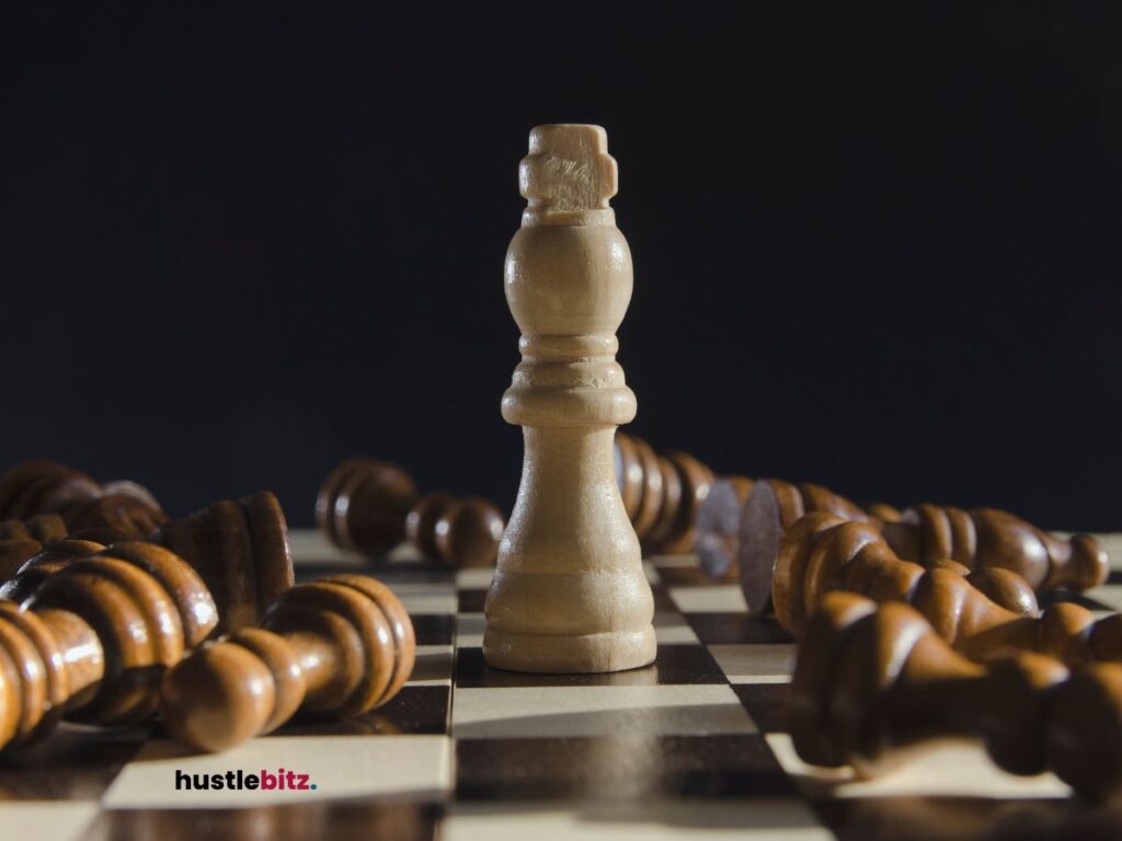 Queen chess piece stands on the chess board surrounded by other pieces knocked down.